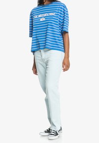 Blå och vit randig kortärmad t-shirt med en logotyp, tillsammans med ljusblå jeans och svarta sneakers. Avslappnad passform och design.