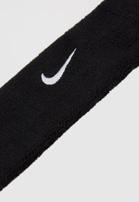 Czarna bawełniana opaska na głowę o fakturowanej powierzchni z białym haftowanym logo Nike. Projekt jest prosty i funkcjonalny.