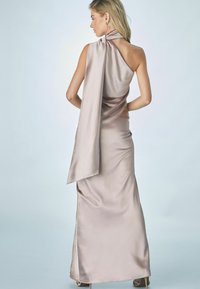 Ljust rosa satin halterneck-klänning med en lång bakre slå, figurnära silhuett och slät, glänsande yta. Enkel design utan dekorationer.