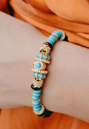 Bracelet en perles turquoise et noires avec des accents dorés, comportant des éléments décoratifs et des détails scintillants, présenté sur un poignet.