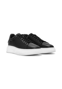 Un paio di sneaker in pelle nera con suole bianche spesse e lacci neri, mostrato da un angolo basso frontale su uno sfondo bianco.