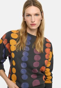 Bluza w ciemnoszarym kolorze z dużymi, wielokolorowymi kropkami w kolorze pomarańczowym, fioletowym i niebieskim. Posiada okrągły dekolt i lekko luźny krój.