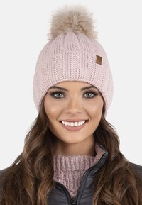 Cască tricotată roz cu un model texturat, cu un pom-pom pufoș pe parte de sus și un mic eticheta logo maron pe lateral.