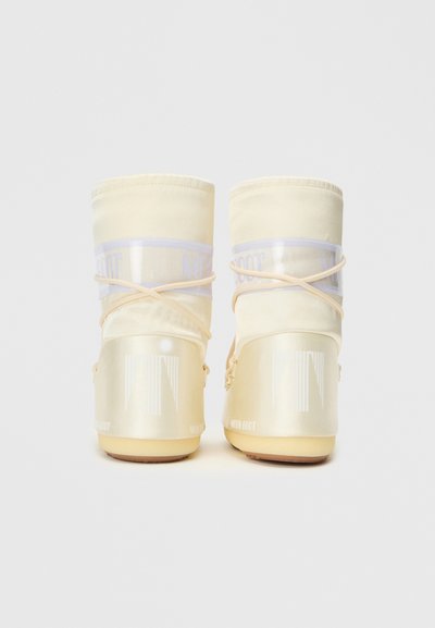 Krémově zbarvené moon boots s průhlednými panely, elastickými tkaničkami a lesklým povrchem; obsahují branding na vnější části paty a horní části.