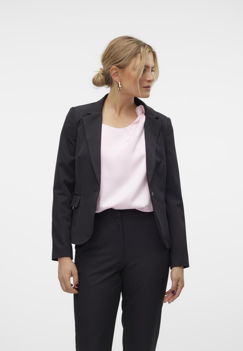 Svart blazer med klaffkragar, en figurformad silhuett och två knappar, kombinert med en mjuk rosa blus och svarta skräddarsydda byxor.