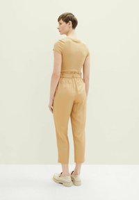 Hellbraunes, tailliertes Oberteil mit kurzen Ärmeln, kombiniert mit hochgeschnittenen, lockeren Hosen in einem ähnlichen Farbton. Chunky-beige Schuhe runden den Look ab.