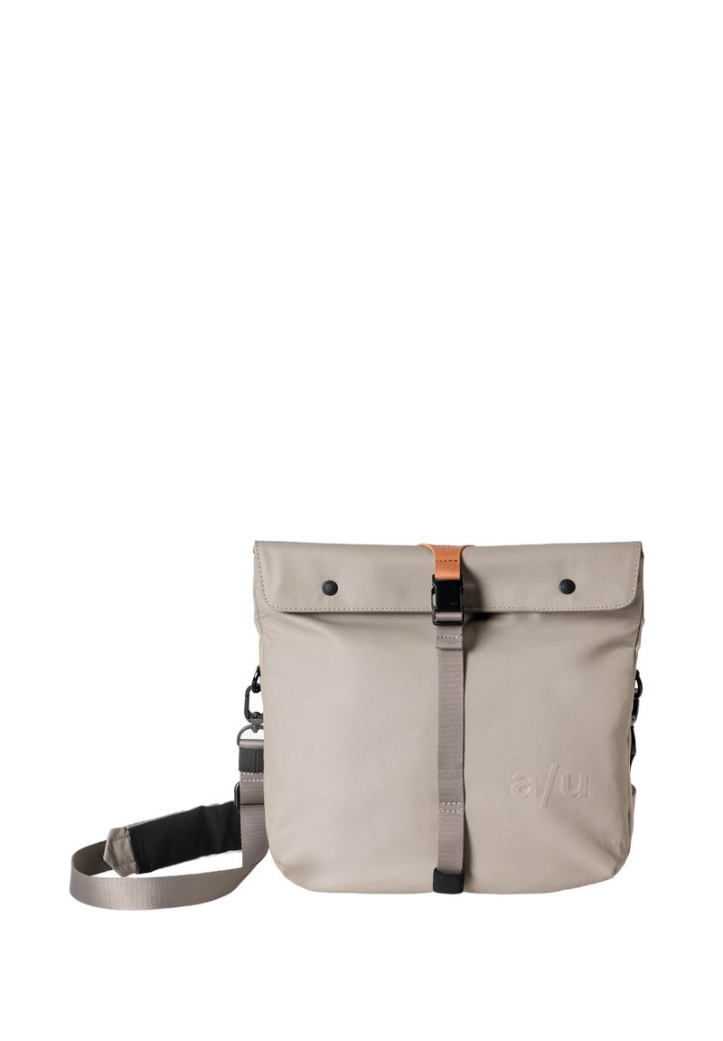 Borsa impermeabile grigia con chiusura a pattina, caratterizzata da un accento in pelle marrone, tracolla regolabile e attacchi laterali. Texture liscia.