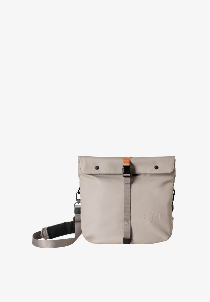 Borsa impermeabile grigia con chiusura a pattina, caratterizzata da un accento in pelle marrone, tracolla regolabile e attacchi laterali. Texture liscia.