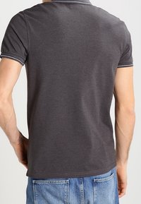 Piké, mörkgrått tyg, kortärmad, krage med vit kant, figursydd design, synlig sömnadsdetalj, buren tillsammans med blå jeans.