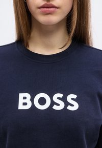 Εκ του κοντά μιας προσωπας που φοράει μια ναυτική μπλούζα με τη λέξη "BOSS" τυπωμένη με μεγάλα λευκά γράμματα στο στήθος.