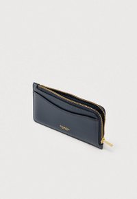 Πορτοφόλι από δέρμα σε ναυτικό μπλε χρώμα με φερμουάρ, που διαθέτει φερμουάρ σε χρυσή απόχρωση και διακριτικό ανάγλυφο λογότυπο στο μπροστινό μέρος. Εξαιρετικά λεπτό και ορθογώνιο σχεδιασμό.