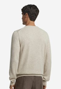 Beżowy sweter z okrągłym dekoltem i długimi rękawami. Miła w dotyku tekstura, ściągacze u rękawów i na dole, minimalistyczny design. Nosi się go na brązowych spodniach.
