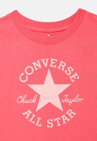 Ροδακινί βαμβακερό t-shirt με μεγάλο λευκό αστέρι και το κείμενο «Converse Chuck Taylor All Star» σε κυκλικό σχέδιο. Απλός στρογγυλός λαιμός.