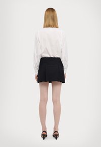 Valkoinen pitkähihaiset paita, jonka hihat ovat ker gathered, yhdistetty mustiin viisivaiheisiin minihameeseen. Mustat korkokengät täydentävät asua.