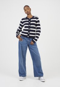 Cardigan en tricot rayé bleu marine et blanc avec un col rond et cinq boutons, associé à un jean en denim bleu clair à coupe ample et des baskets blanches.