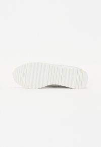 Valge sneakerite tallaga, millel on tekstuuriga ja sooneline disain. Siledat pinda iseloomustavad minimalistlikud detailid; ümardatud varbaosa voolab sujuvaks kujuks.