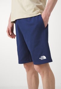 Shorts di cotone blu navy con vita elastica, tasche laterali e un logo bianco de "The North Face" sull'orlo inferiore.