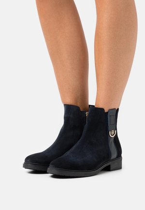 Navy blue suede ankle boots with a side zipper, rounded toe, and a small block heel. Gold hardware accent on the zipper.