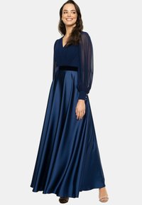 Granatowa satynowa sukienka maxi z głębokim dekoltem, przezroczystymi długimi rękawami i aksamitnym pasem w talii. Posiada zwiewną spódnicę z guziczkami przy mankietach.