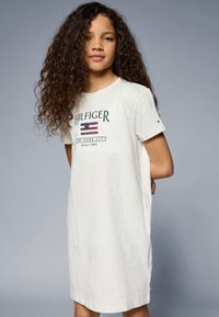 Svetlosivý bavlnený šaty v štýle trička s krátkymi rukávmi. Obsahuje potlačené námornícke modré logo "HILFIGER" a dizajn vlajky. Uvoľnený strih s bočnými vreckami.