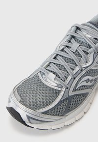Grauer Sportschuh aus Mesh-Material, mit einem strukturierten Design, Schnürsenkeln und einer gedämpften Sohle. Auffällige silberne Akzente und Logo-Details.