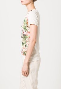 T-shirt med blomstermønster i cremet bomuld, korte ærmer, tætsiddende form, med en blød tekstur og ribbet kant, båret med lyse bukser.