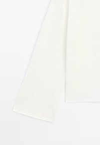 Pull en maille blanc à manches longues avec texture côtelée, montré de côté, mettant en valeur la manche droite et le design simple.