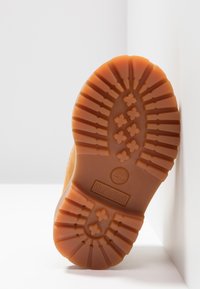 Brun gummisål med et dækmønster, der har et Timberland-logo. Sålen viser riller og cirkulære greb til traction.