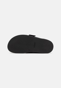 Semelle de sandale noire avec un motif de grip texturé, présentant une forme arrondie et le mot « PAVEMENT » en relief près du talon. Taille 37 indiquée.