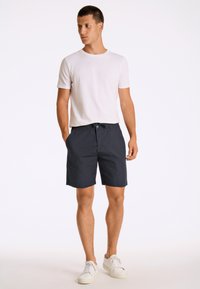 Marinblå shorts med resårband i midjan och framfickor, kombinerat med en enkel vit T-shirt med rundad halsringning och vita sneakers.