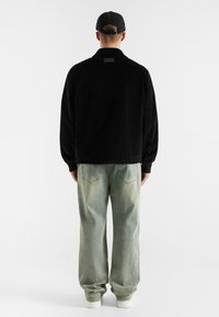 Black corduroy jacket with a collar, long sleeves, and a rectangular accent on the back, paired with light blue baggy jeans.