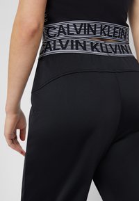 Czarne spodnie sportowe z teksturowanym wykończeniem, z kontrastowym ściągaczem z logo Calvin Klein w czarno-białe paski.