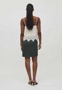 Bílý texturovaný top s krajkovým lemem, v kombinaci s tmavozelenou přiléhavou sukní. Nosit s černými sandály na otevřenou špičku. Vlasy jsou dlouhé a rovné.