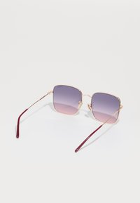 Ochelari de soare pătrați cu cadru din metal auriu, lentile degradate violet și brațe bordo; prezintă detalii decorative pe cadru.