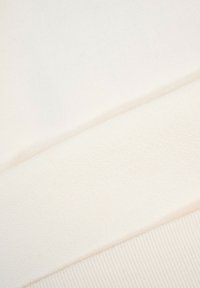 Trzy zbliżenia sekcji tkaniny w odcieniach off-white o różnych strukturach i wzorach dzianinowych, ułożone diagonalnie.