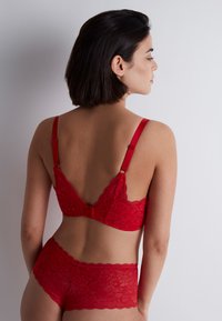 Soutien-gorge en dentelle rouge et culotte assortie, ornés de motifs floraux, avec des bretelles ajustables et une fermeture par crochets au dos.