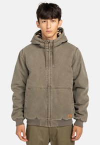 Veste marron à capuche avec fermeture éclair sur le devant, poignets et ourlet côtelés. Équipée de grandes poches avant et d'une doublure intérieure à carreaux. Texture de tissu durable.