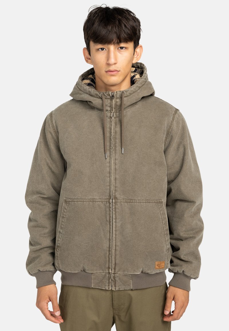 Giacca marrone con cappuccio, chiusura a zip, polsini e orlo a coste. Presenta grandi tasche frontali e un rivestimento interno a quadri. Tessuto robusto.