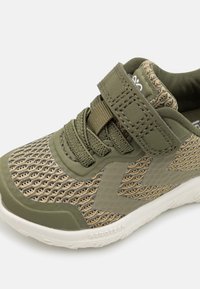 Olive green and beige child’s sneaker with mesh fabric, thick laces, a Velcro strap, and white rubber sole with “AEROTECH” branding.