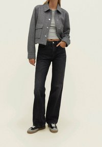 Szara kurtka o fakturze w jodełkę, skrócona, z kieszeniami z przodu, w połączeniu z czarnymi dżinsami o wysokim stanie i szarymi trampkami. Prosty, casualowy design.