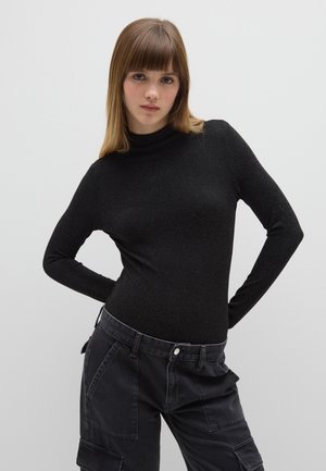 Top negro de manga larga con cuello alto y una textura ligeramente brillante, combinado con pantalones cargo negros de talle alto, holgados y con bolsillos laterales.