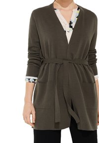 Cardigan tricoté vert olive avec un design enroulé, ceinture à nouer, deux poches sur le devant et des poignets à motifs de couleurs claires qui émergent des manches.