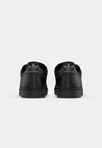 Black Adidas sneakers with smooth leather texture, featuring a low-top design and subtle three-stripe detail. Logo displayed on heel.