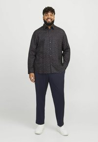 Chemise à manches longues à motif sombre avec une base bleu marine, ornée de petits motifs floraux colorés. Assortie à un pantalon à rayures bleu marine et des baskets blanches.