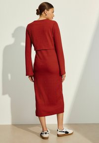 Langärmliges, geripptes Kleid in Dunkelrot mit einem kurzen Oberteil und einem knielangen Rock, kombiniert mit weißen und schwarzen Turnschuhen. Glatte Textur.