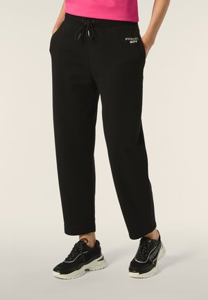 Pantalons de survêtement noirs avec taille à cordon, poches latérales et détail de logo. Associés à des baskets noires avec semelles et accents blancs.