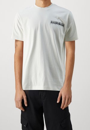 Man wearing white Napapijri Geographic t-shirt and black cargo pants, standing against plain light background.