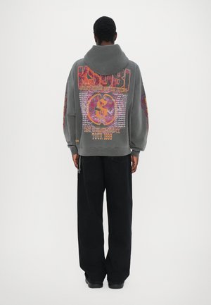 Gray oversized hoodie with vibrant printed graphics on the back, paired with loose black pants. Features a drawstring hood and ribbed cuffs.