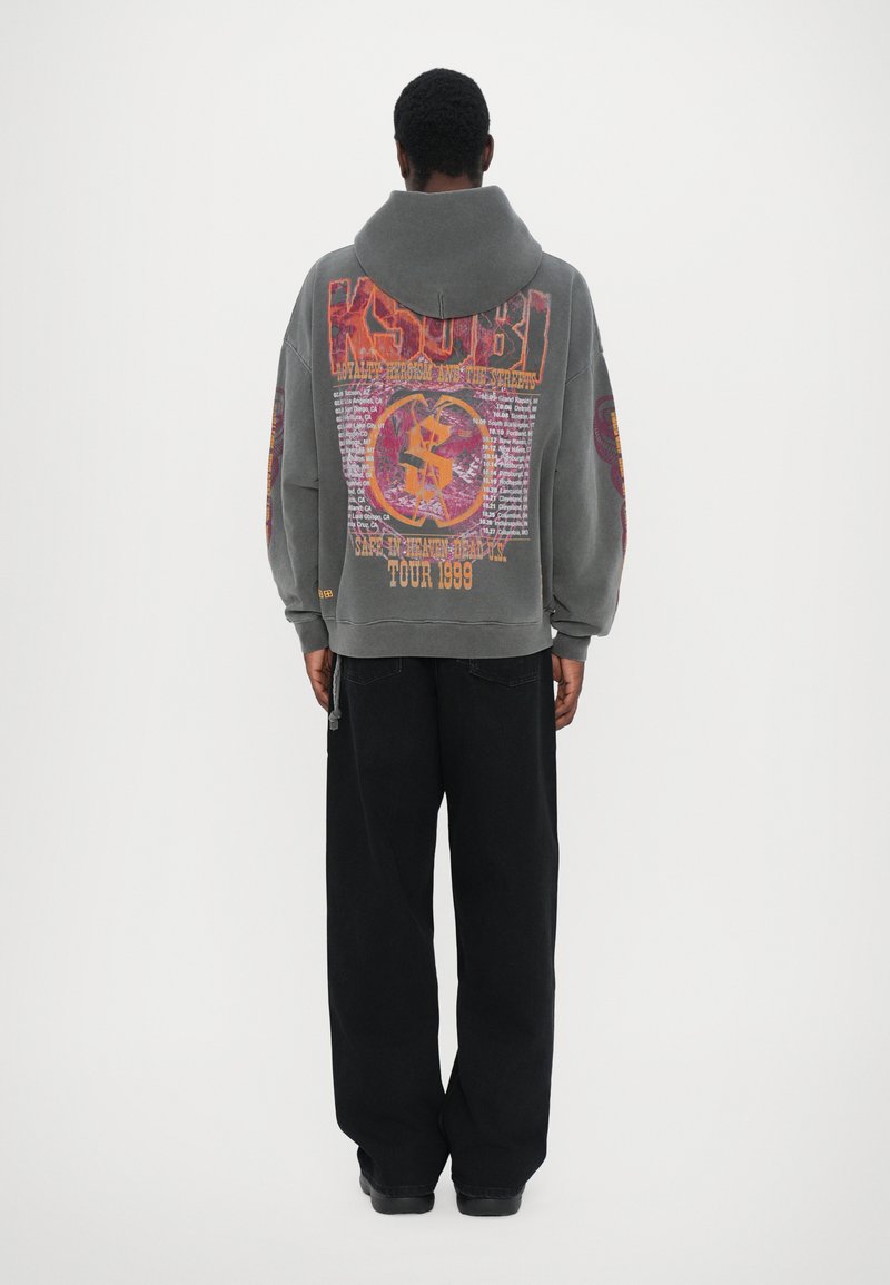 Sweat-shirt à capuche surdimensionné gris avec des graphiques imprimés vibrants au dos, associé à un pantalon noir ample. Il comprend une capuche avec cordon de serrage et des poignets côtelés.