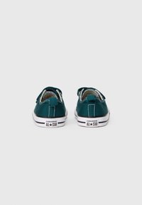 Pár tmavozelených nízkych tenisiek Converse All Star z pohľadu zozadu na jednoduchom bielom pozadí.